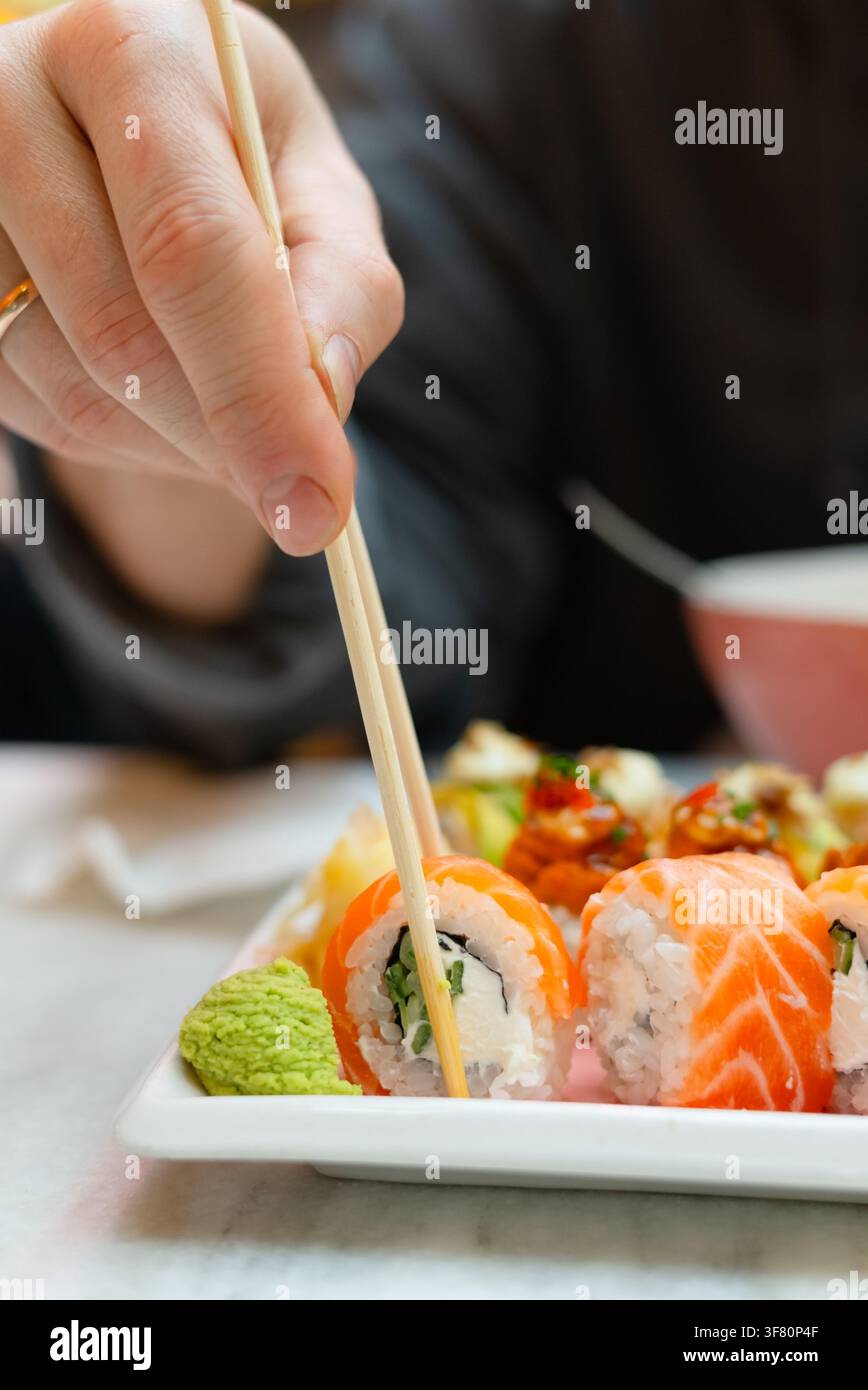 Homme savourant un délicieux repas de sushi à une table de restaurant confortable. Amateur de nourriture appréciant des roulés frais avec une satisfaction chaleureuse. Moment de réconfort avec une cuisine japonaise et une atmosphère conviale Banque D'Images