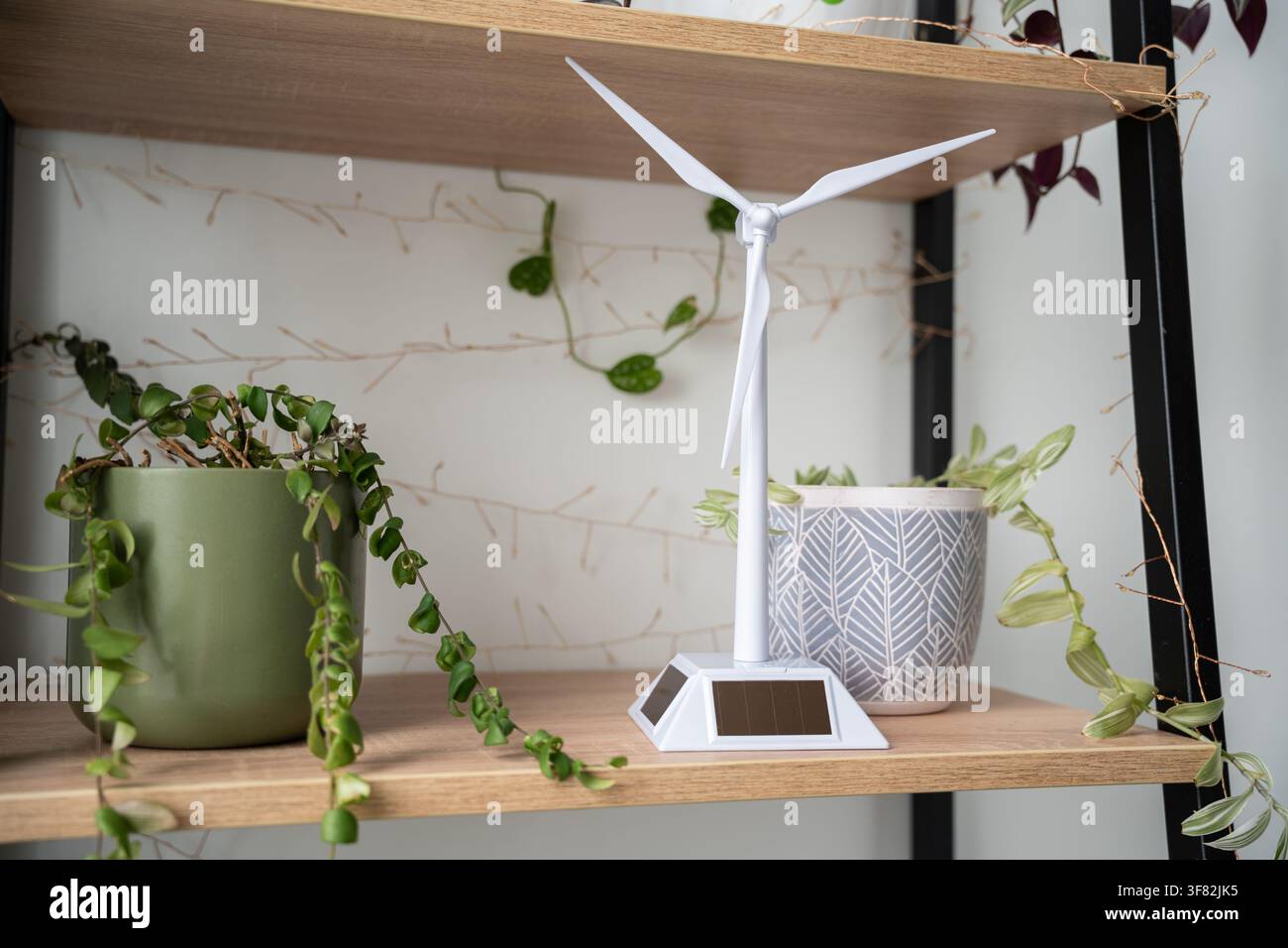 Modèle d'éolienne miniature exposé sur une étagère en bois avec des plantes d'intérieur luxuriantes. Concept d'éducation aux énergies renouvelables et de décoration durable de la maison. Banque D'Images