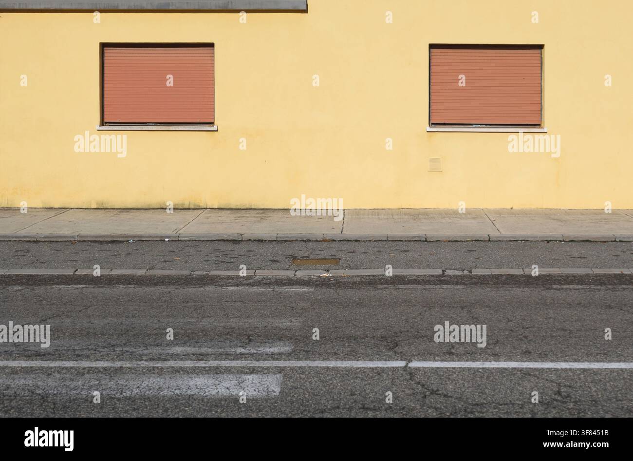 Façade en plâtre jaune avec deux volets bruns fermés. Trottoir, rue et marquage de passage piétonnier usé devant. Fond pour espace de copie Banque D'Images