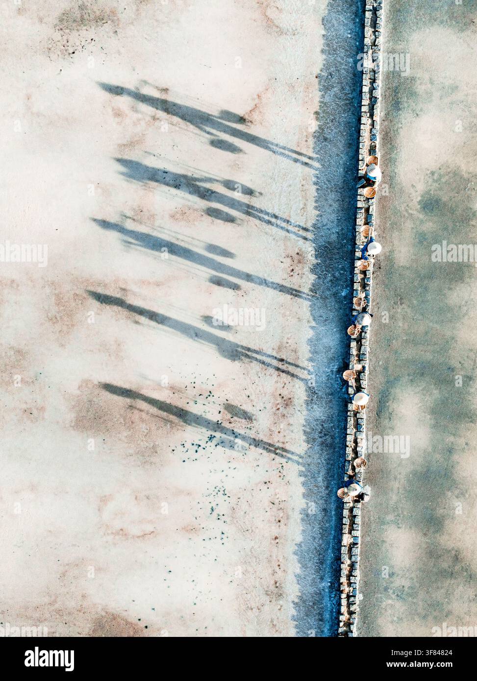 Des ouvriers traversent des champs de sel, projetant de longues ombres dans la province de Hon Khoi Khanh Hoa au Vietnam pendant la saison des récoltes Banque D'Images
