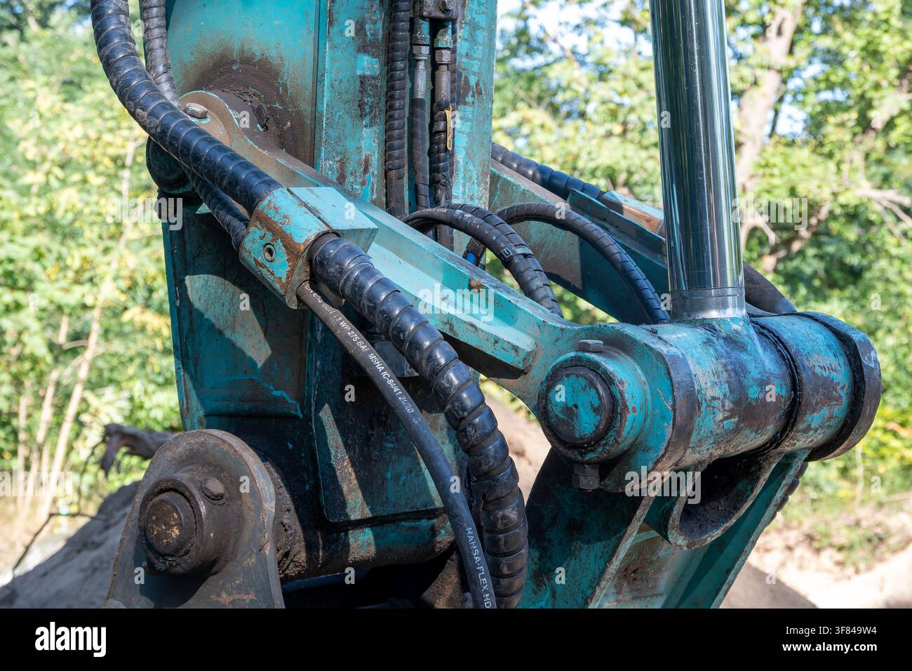 Un gros plan détaillé du bras mécanique et des tuyaux hydrauliques d'une pelleteuse bleu-vert travaillant sur un chantier forestier. Banque D'Images