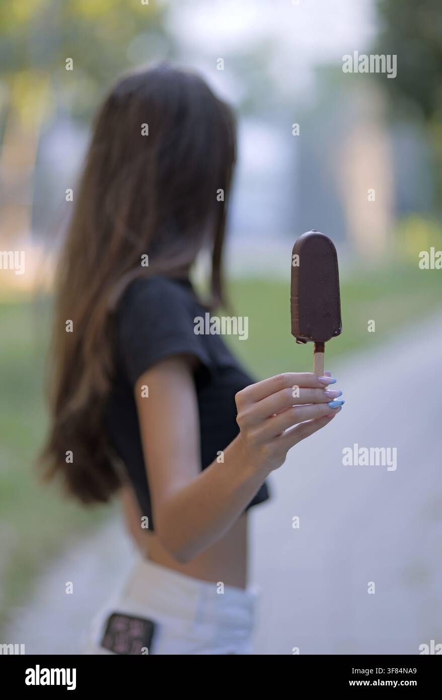 Jeune femme tenant une barre de glace au chocolat rafraîchissante par le bâtonnet, savourant une douce collation pendant une chaude journée d'été dans un cadre de parc Banque D'Images