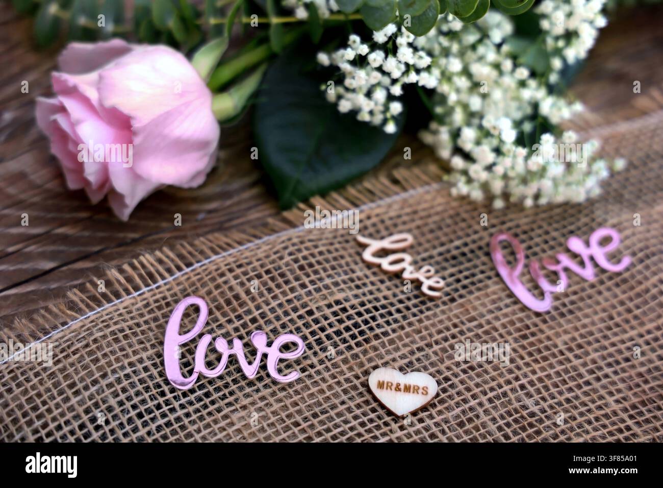 Rose rose et Gypsophila paniculata (boule de neige) avec panneau d'amour sur une décoration de mariage rustique en toile de jute Banque D'Images