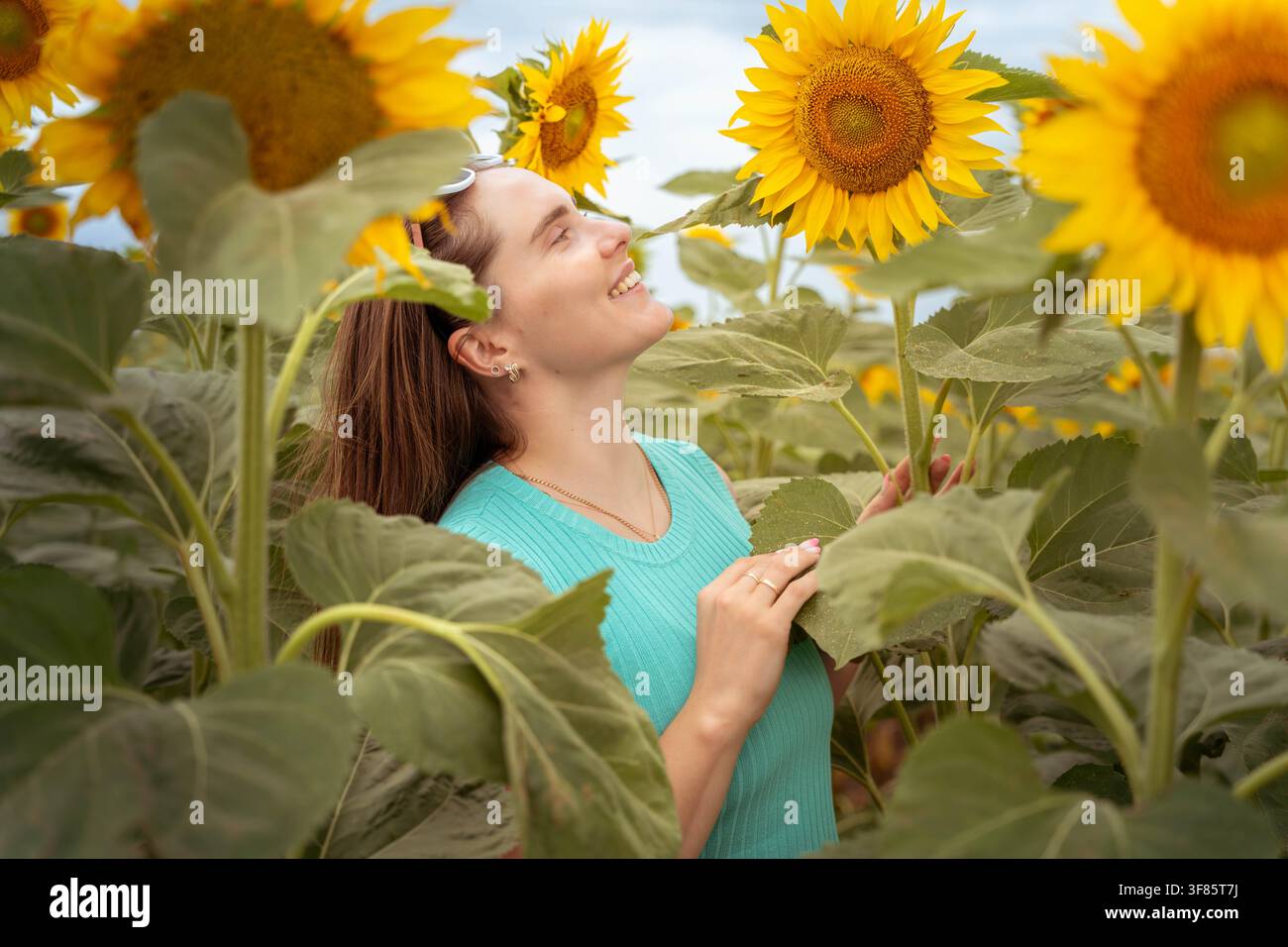 Femme souriant et regardant les tournesols, dans un champ de tournesols, avec des tournesols, vêtements de femme, d'une perspective de niveau oculaire en gros plan Banque D'Images