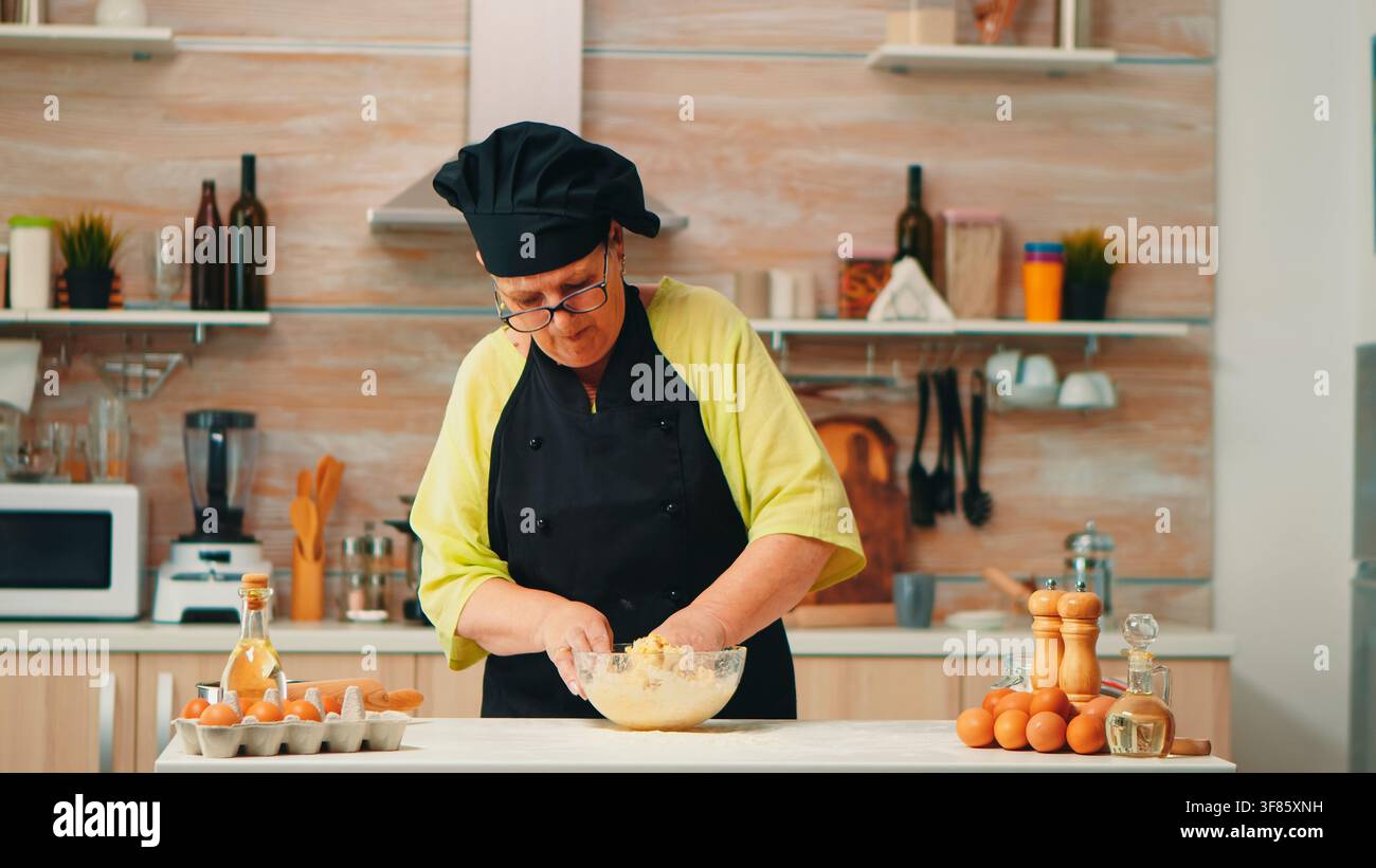 Le processus de cuisine maison se poursuit avec le mélange à la main d'œufs, de farine et d'autres ingrédients pour la pâtisserie, à une table préparée pour la pâtisserie maison avant la cuisson maison. Banque D'Images