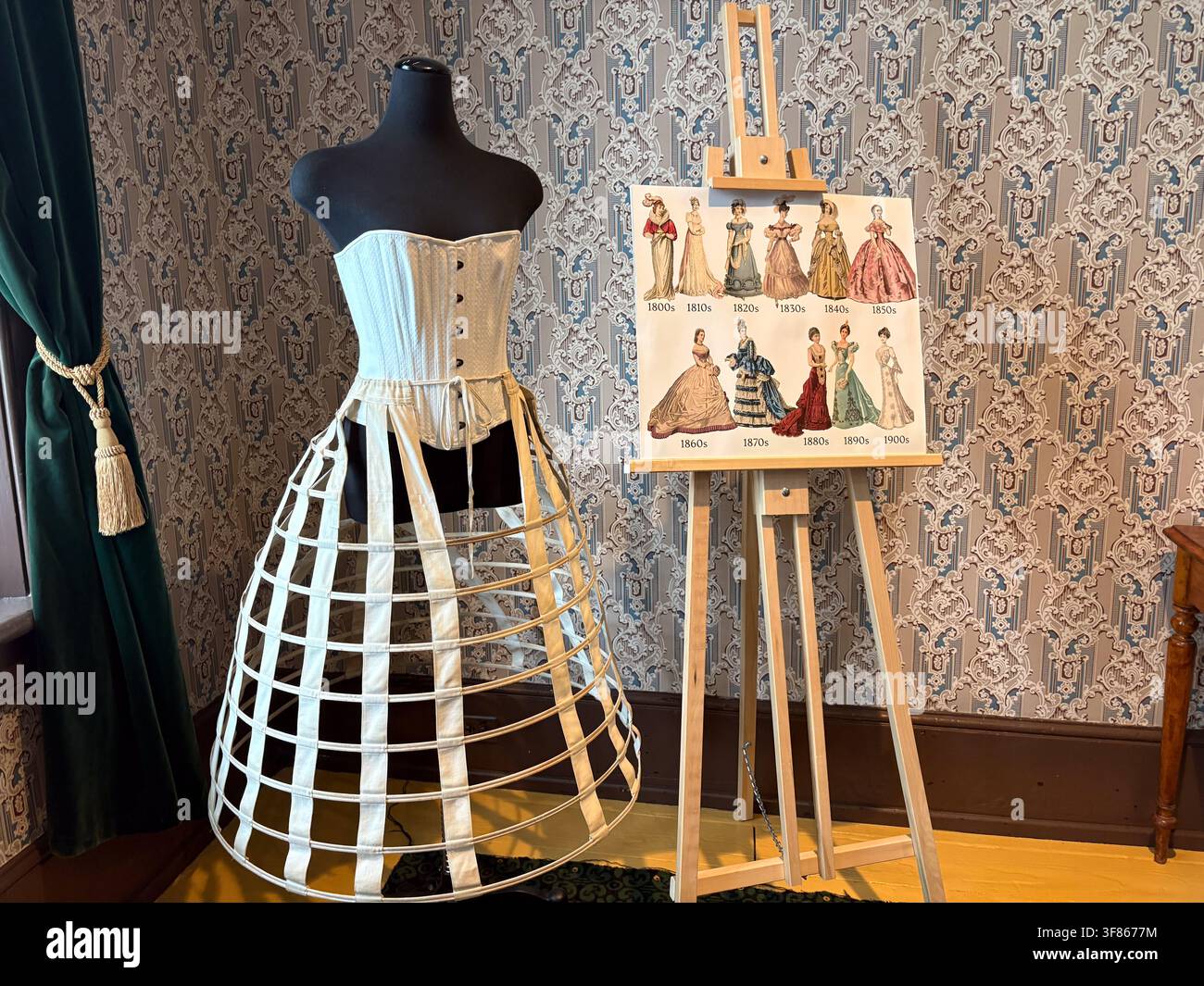 Exposition d'un corset et d'une jupe en cage à crinolines du XIXe siècle sur un mannequin noir à côté d'un chevalet d'illustration de mode. Banque D'Images