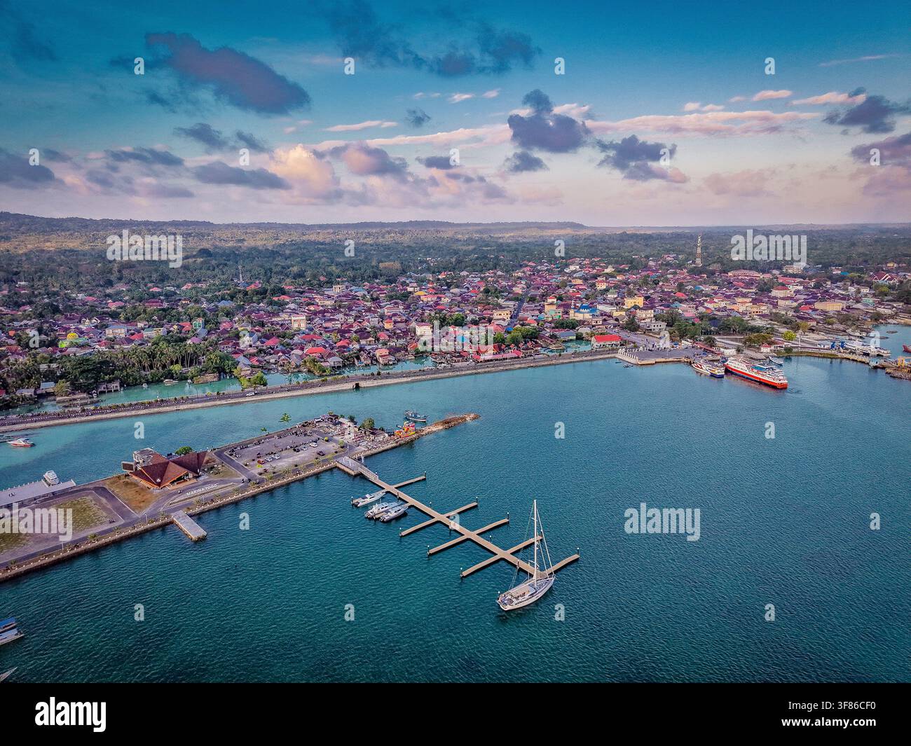 Vue aérienne de l'île de Wangiwangi montrant la ville côtière de Wakatobi avec sa marina, son voilier, sa jetée et son paysage tropical luxuriant sous un ciel bleu Banque D'Images