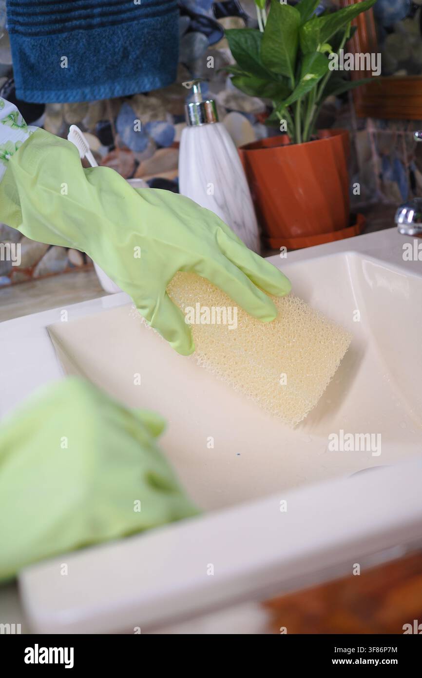 Nettoyage d'un évier avec une éponge et des gants dans une cuisine Banque D'Images
