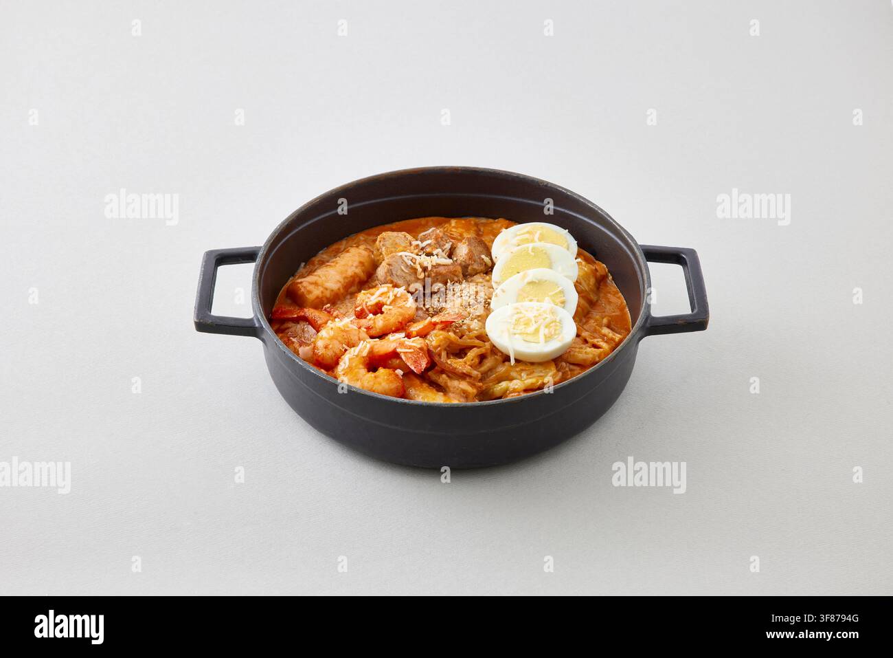 Frites épicées coréennes de crevettes et fruits de mer avec œuf bouilli servi dans une poêle en fonte noire sur un fond gris clair, photographie de nourriture de restaurant coréen Banque D'Images