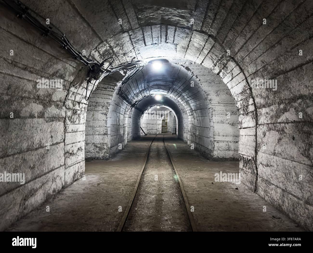 Tunnel souterrain de mine de charbon avec voies ferrées, les murs de pierre rugueuse ajoutent à l'atmosphère sombre et mystérieuse de ce passage abandonné Banque D'Images