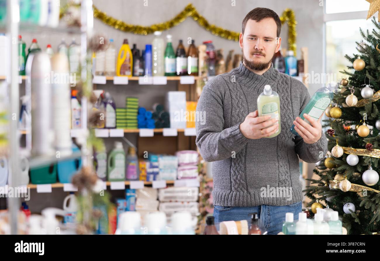 Client choisissant le liquide vaisselle dans un magasin de ménage décoré de façon festive Banque D'Images