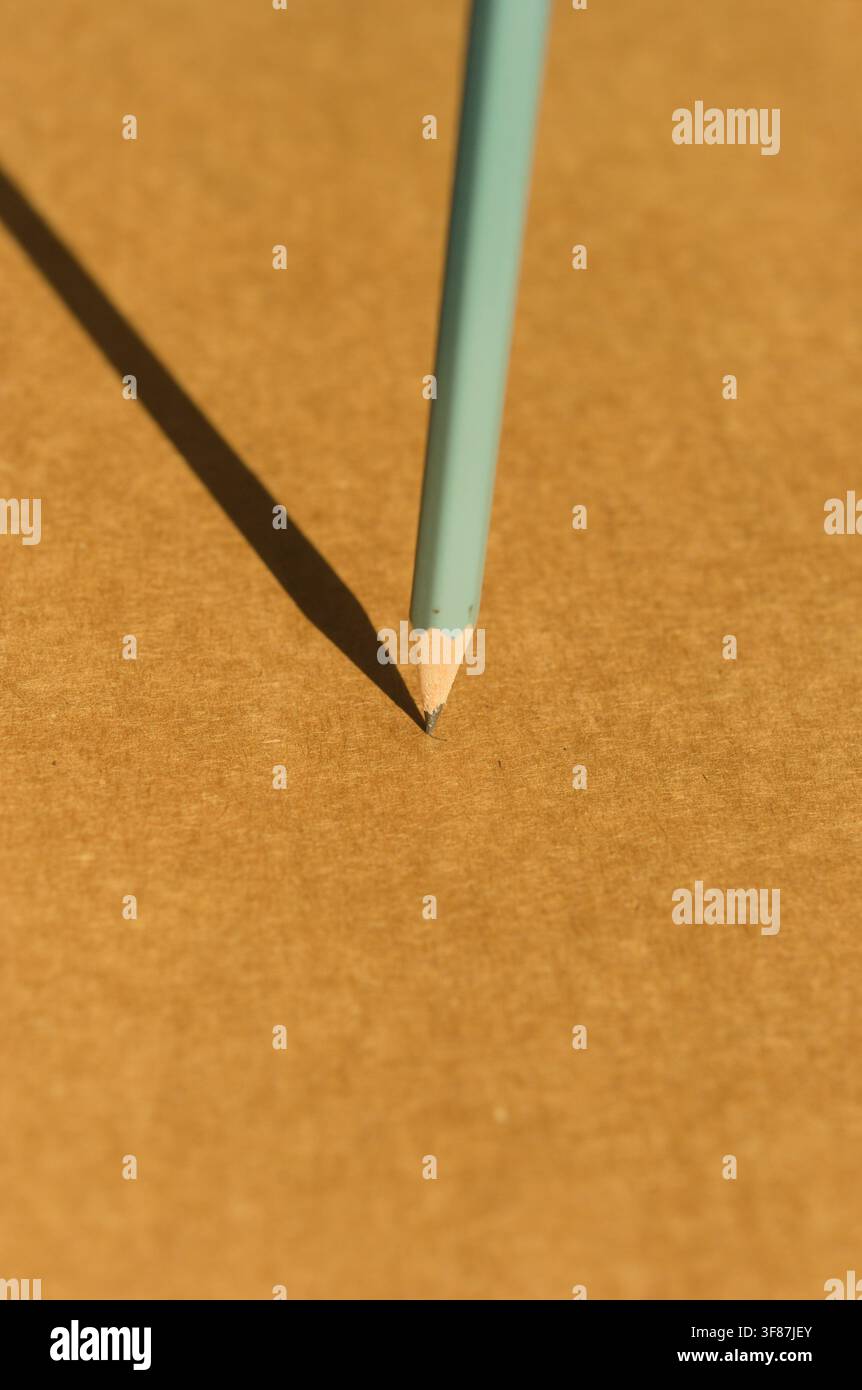 Crayon vert menthe affûté posé pointe vers le bas sur une surface ocre chaude, projetant une longue ombre dramatique sous le soleil Banque D'Images