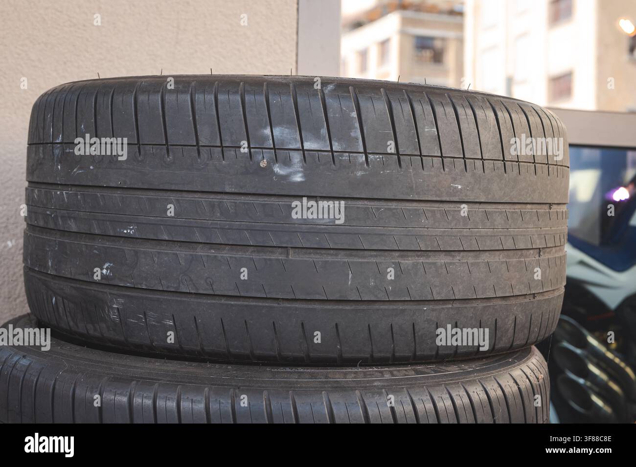 Plan rapproché au niveau des yeux détaillant le motif de la bande de roulement, les canaux d'eau profonds et la texture du caoutchouc des pneus automobiles empilés à l'extérieur près d'une éolienne d'atelier Banque D'Images