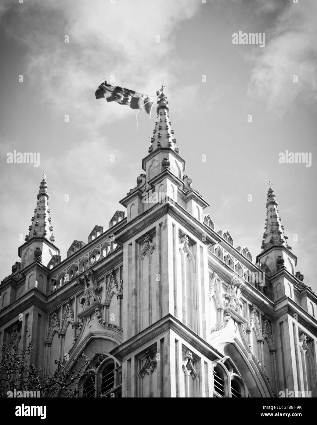 Vue aérienne d'une église gothique historique avec des flèches de pierre complexes et un drapeau flottant contre un ciel nuageux à Londres, Angleterre, Royaume-Uni. Banque D'Images