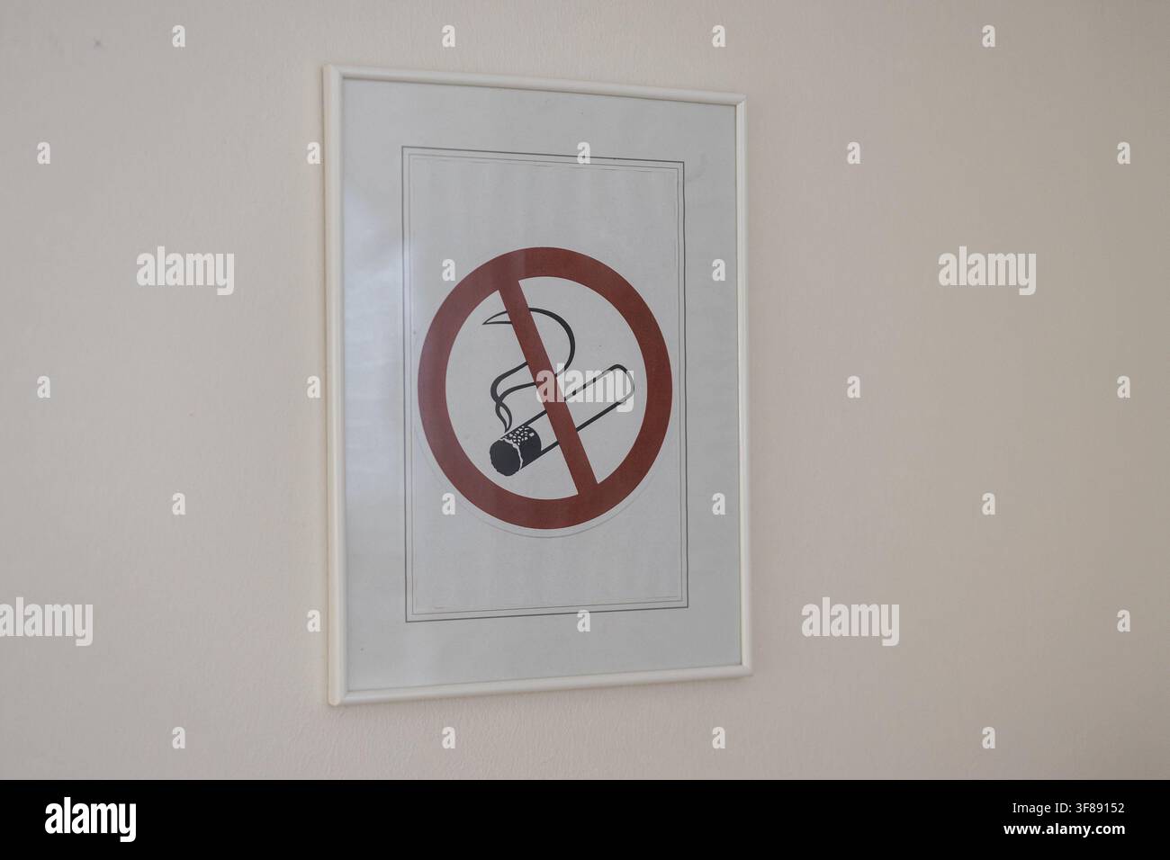 Un panneau «interdiction de fumer» encadré présentant un cercle de prohibition rouge classique au-dessus d'une cigarette allumée, fixé sur un mur blanc simple dans un environnement intérieur. Banque D'Images