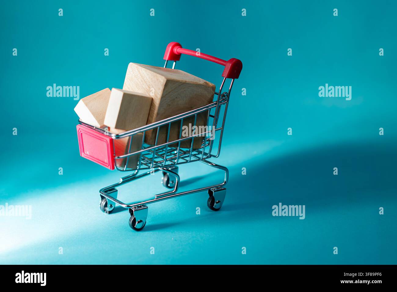 Un mini chariot de courses rempli de blocs de bois simples sur une surface bleu cyan représentant la livraison de marchandises et les transactions de commerce électronique. Photo de haute qualité Banque D'Images