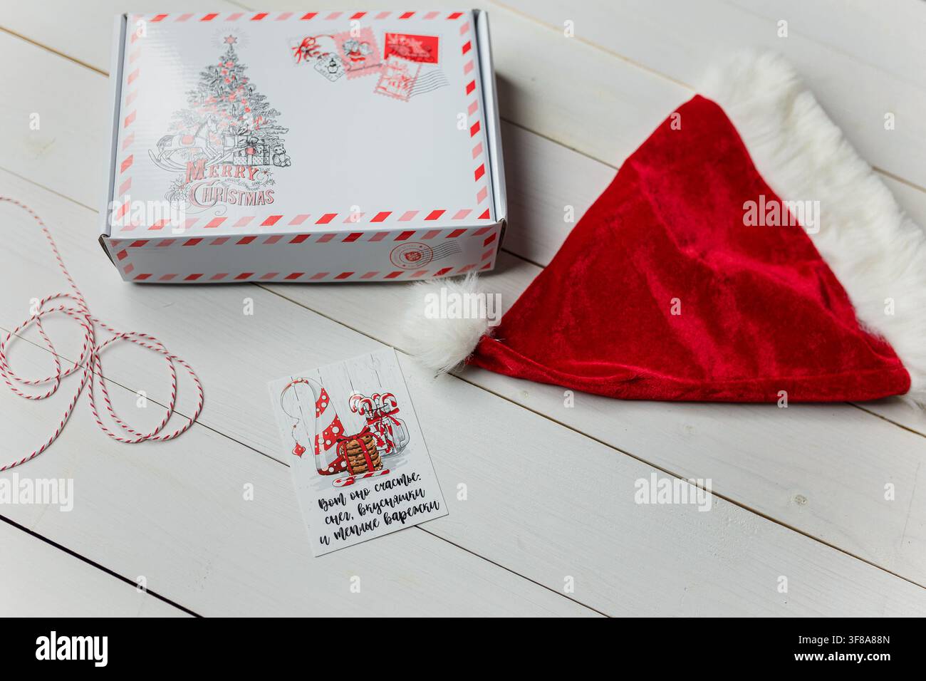 Izmail, Ukraine – 13 décembre 2019. Cadeau de Noël, chapeau du Père Noël sur une table en bois blanc. Inscription sur la carte : Le bonheur est la neige, les bonbons et les gants chauds Banque D'Images
