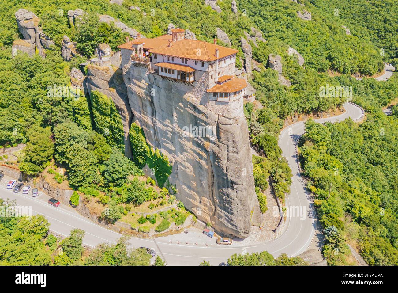 Vue aérienne par drone du monastère de Rousanou perché sur une falaise verticale avec une route asphaltée sinueuse en contrebas par une journée ensoleillée dans la région de Météora à Kalambaka T Banque D'Images