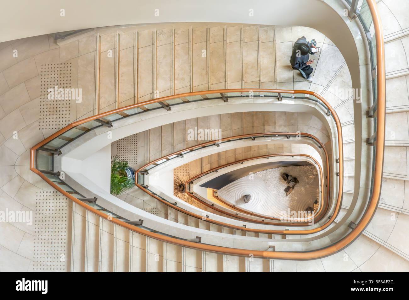 Vue de l'élégante escalier en colimaçon du Peninsula Tokyo avec une personne descendant et un jardin zen minimaliste visible à la base à Chiyoda City Banque D'Images