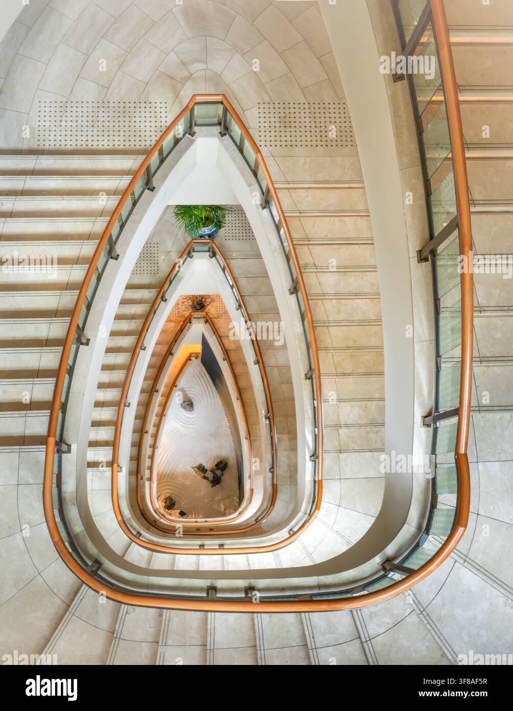 Vue de l'élégante escalier en colimaçon du The Peninsula Tokyo, avec des marches en pierre polie et une rampe en bois incurvée, regardant vers le bas dans le lumineux Banque D'Images
