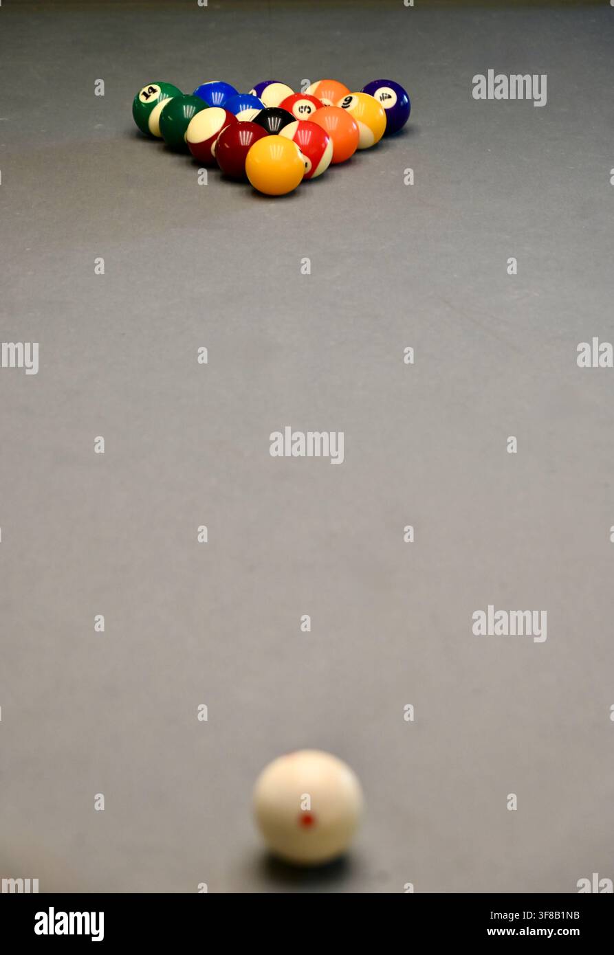 Photographie commerciale en vue plongeante d'un ensemble de boules de billard colorées disposées sur un rack et d'une boule blanche positionnée sur une table de billard grise et élégante, prête pour une partie. Banque D'Images