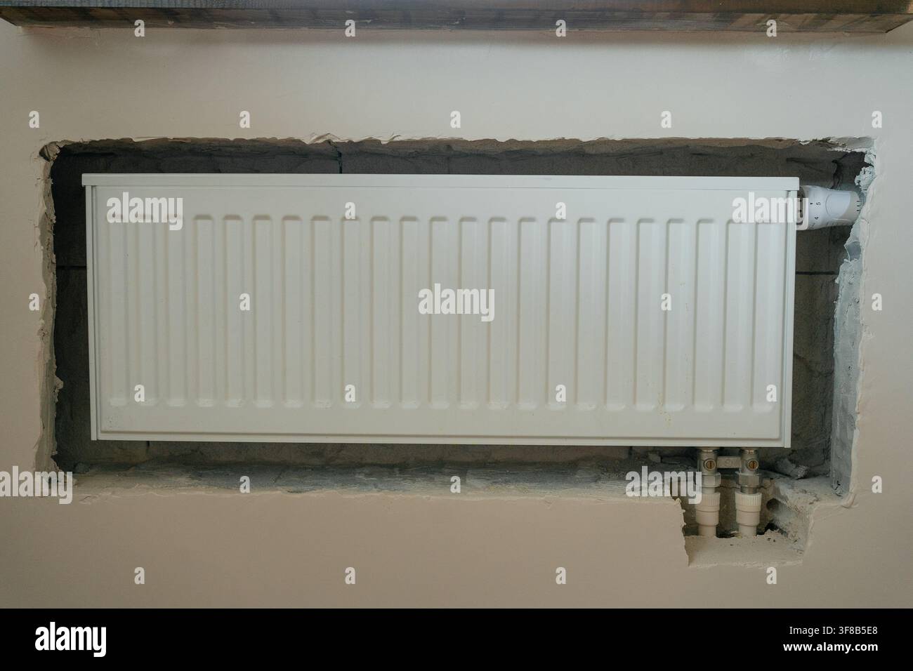 Radiateur blanc horizontal installé dans une niche murale non vernie lors de la rénovation de la pièce. Photo de stock idéale pour l'amélioration de l'habitat, la plomberie Banque D'Images