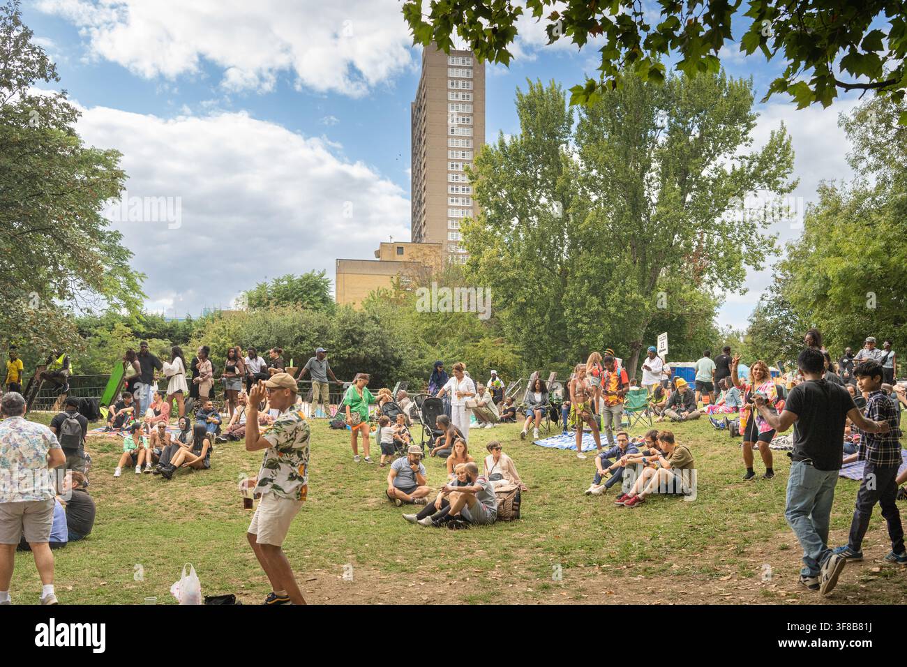 Les foules profitent d'une pause au Carnaval de Notting Hill 2022, se relaxant sur l'herbe avec l'emblématique tour Trellick visible en arrière-plan. Banque D'Images