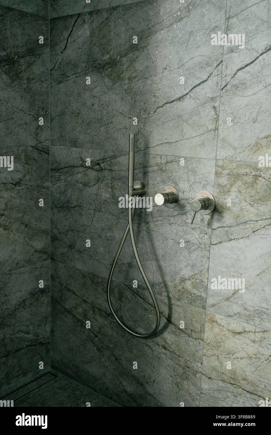 Ensemble de douchette chromée avec sortie murale et mitigeur minimaliste dans une cabine de douche carrelée en pierre sombre. Image parfaite pour une salle de bain luxueuse Banque D'Images