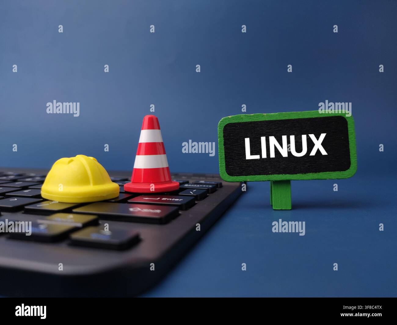 Un casque de sécurité miniature jaune, un cône de signalisation et un panneau portant l'inscription LINUX reposent sur un clavier d'ordinateur sombre. Banque D'Images