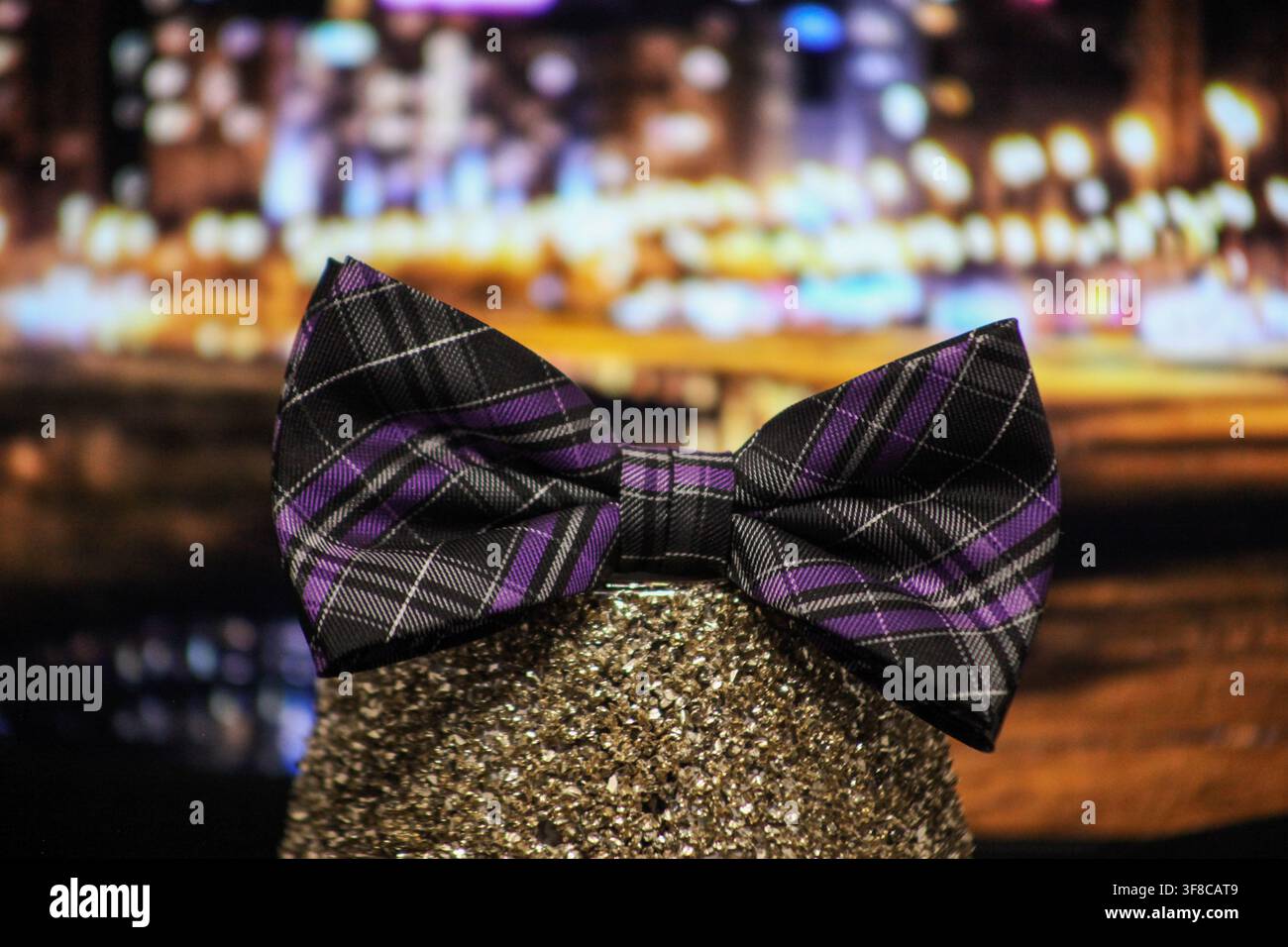 Nœud papillon à motif écossais violet et noir affiché contre des lumières floues colorées. Banque D'Images
