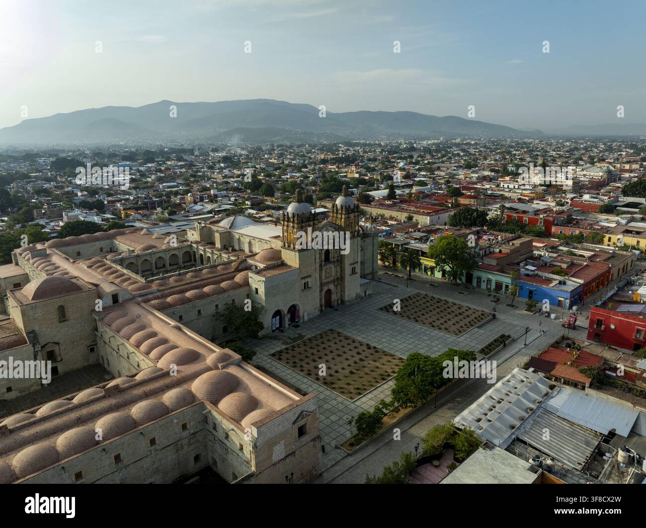 Vue aérienne du temple historique de Santo Domingo de Guzman avec une façade ornée et des dômes, surplombant les toits de la ville coloniale et les montagnes d'Oaxaca Banque D'Images