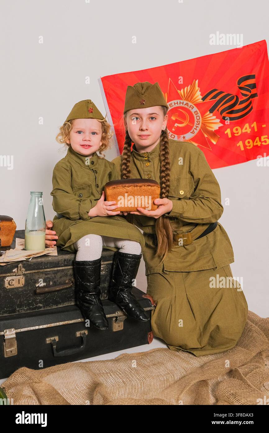 Femme et fille en uniforme militaire vintage tenant du pain. Célébration de la Journée de la Victoire avec une affiche de propagande soviétique. Réenactement historique. Banque D'Images