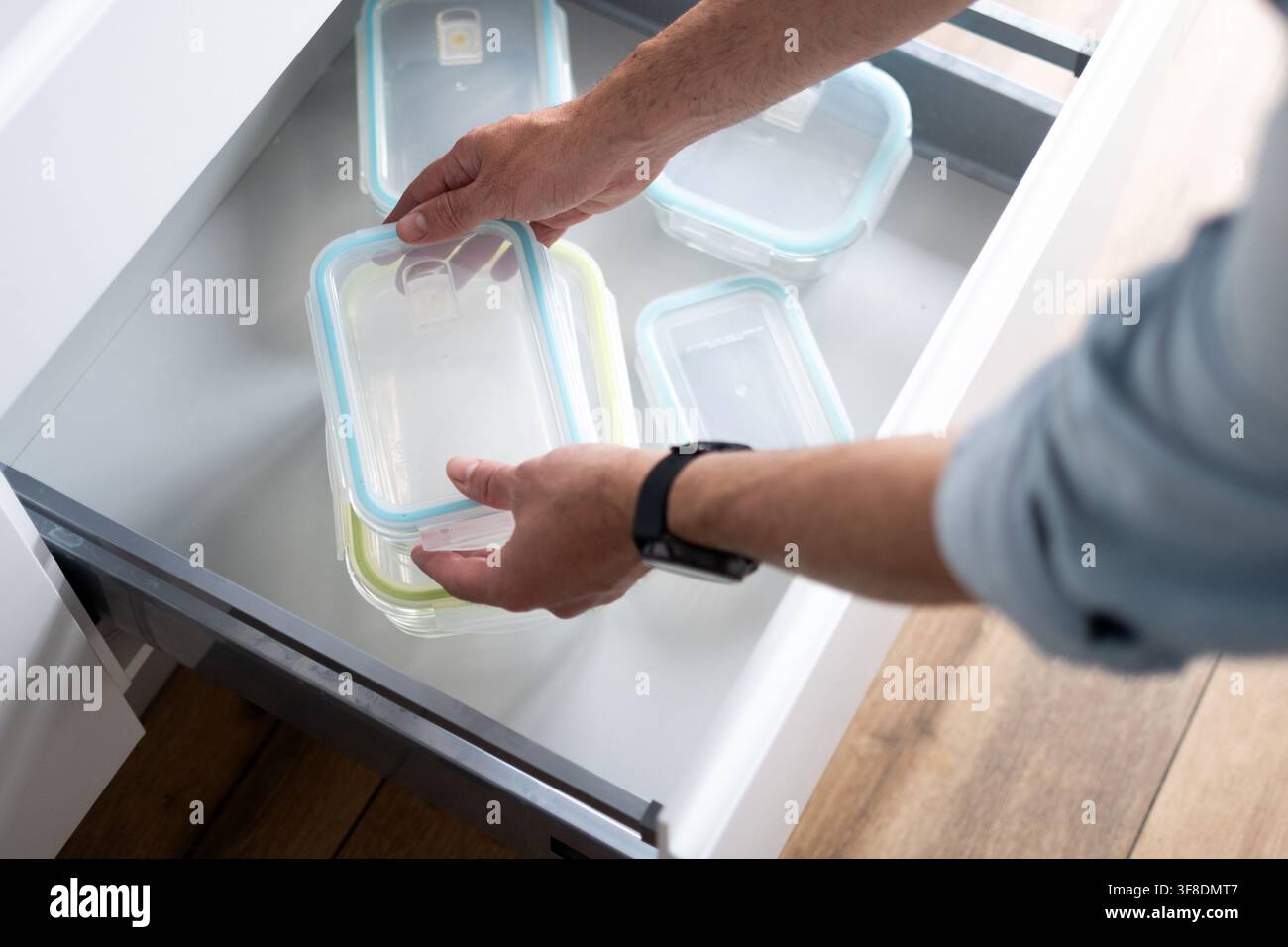 Homme tenant un récipient de stockage alimentaire réutilisable propre après l'avoir pris dans un tiroir de cuisine organisé, prêt pour la préparation des repas. Banque D'Images