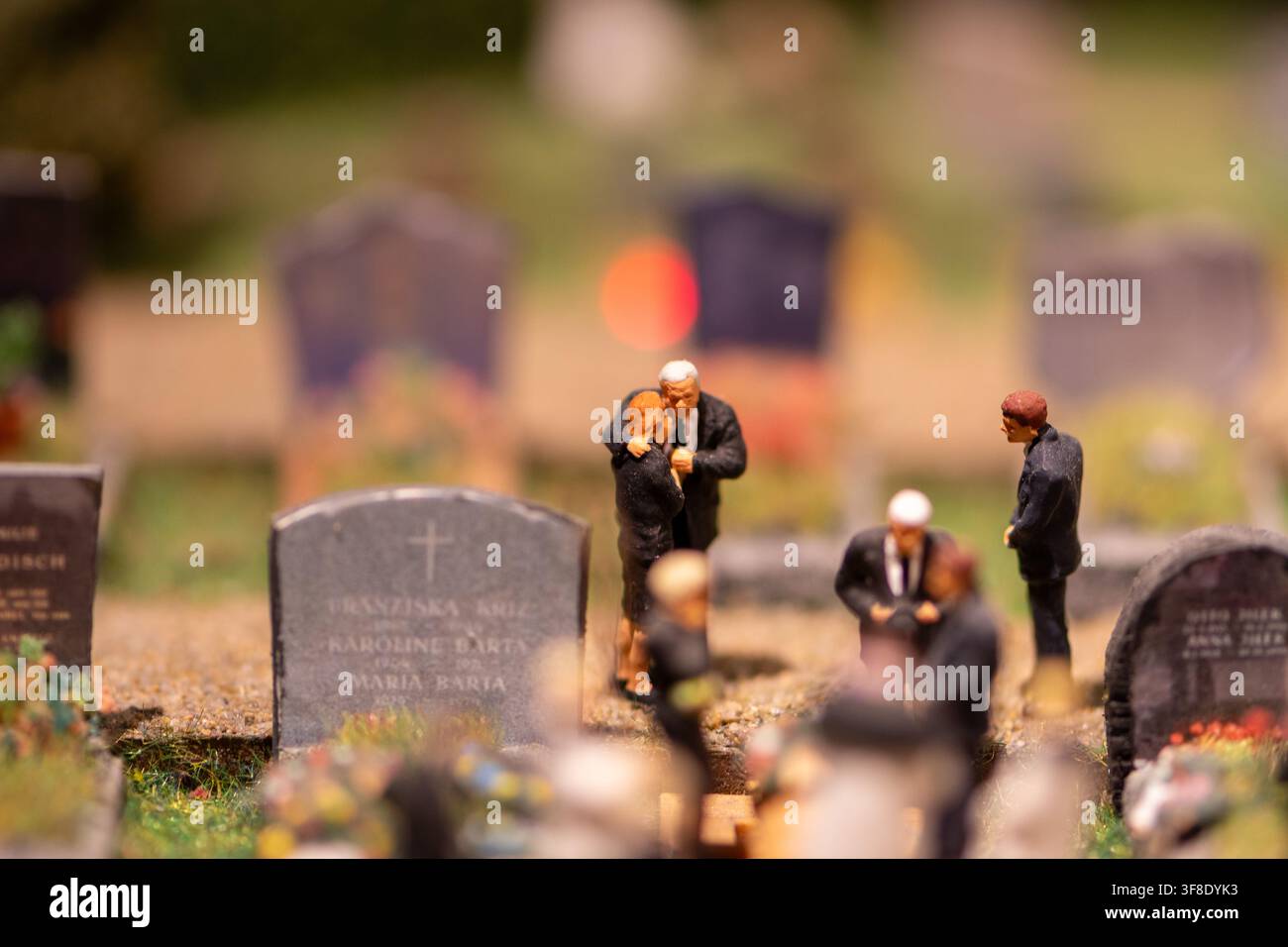 De minuscules figurines de pleureurs se dressent parmi les pierres tombales dans une scène de cimetière miniature avec mise au point sélective. Banque D'Images