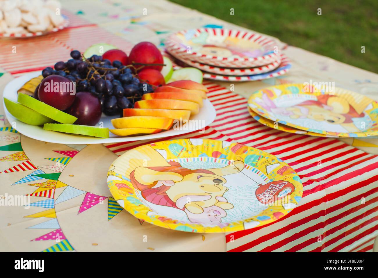 Des fruits frais et des assiettes en carton colorées sont disposés sur une table de fête en plein air. Banque D'Images