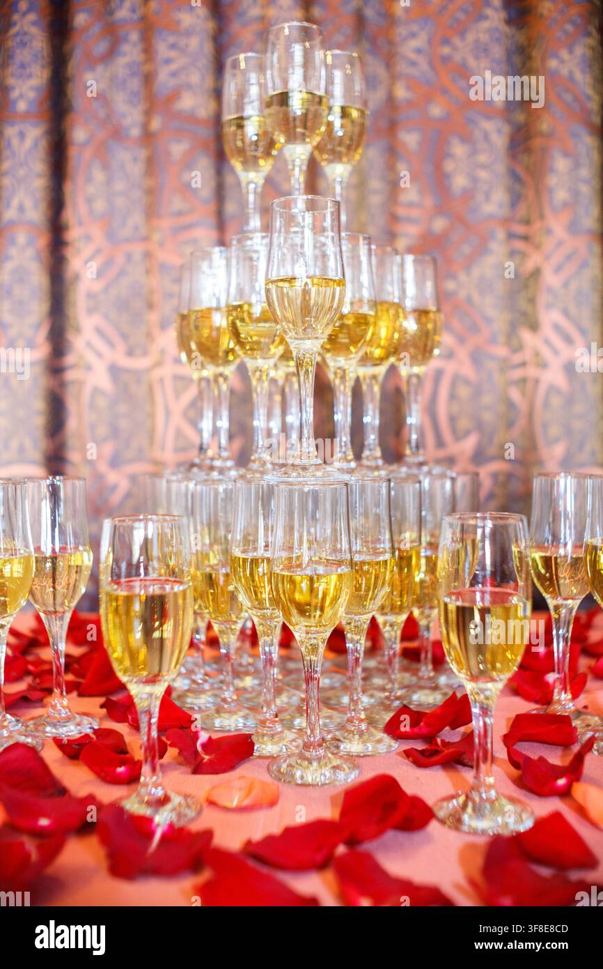 Une magnifique pyramide de champagne se dresse entourée de pétales de rose rouges éparpillés sur une table. Banque D'Images