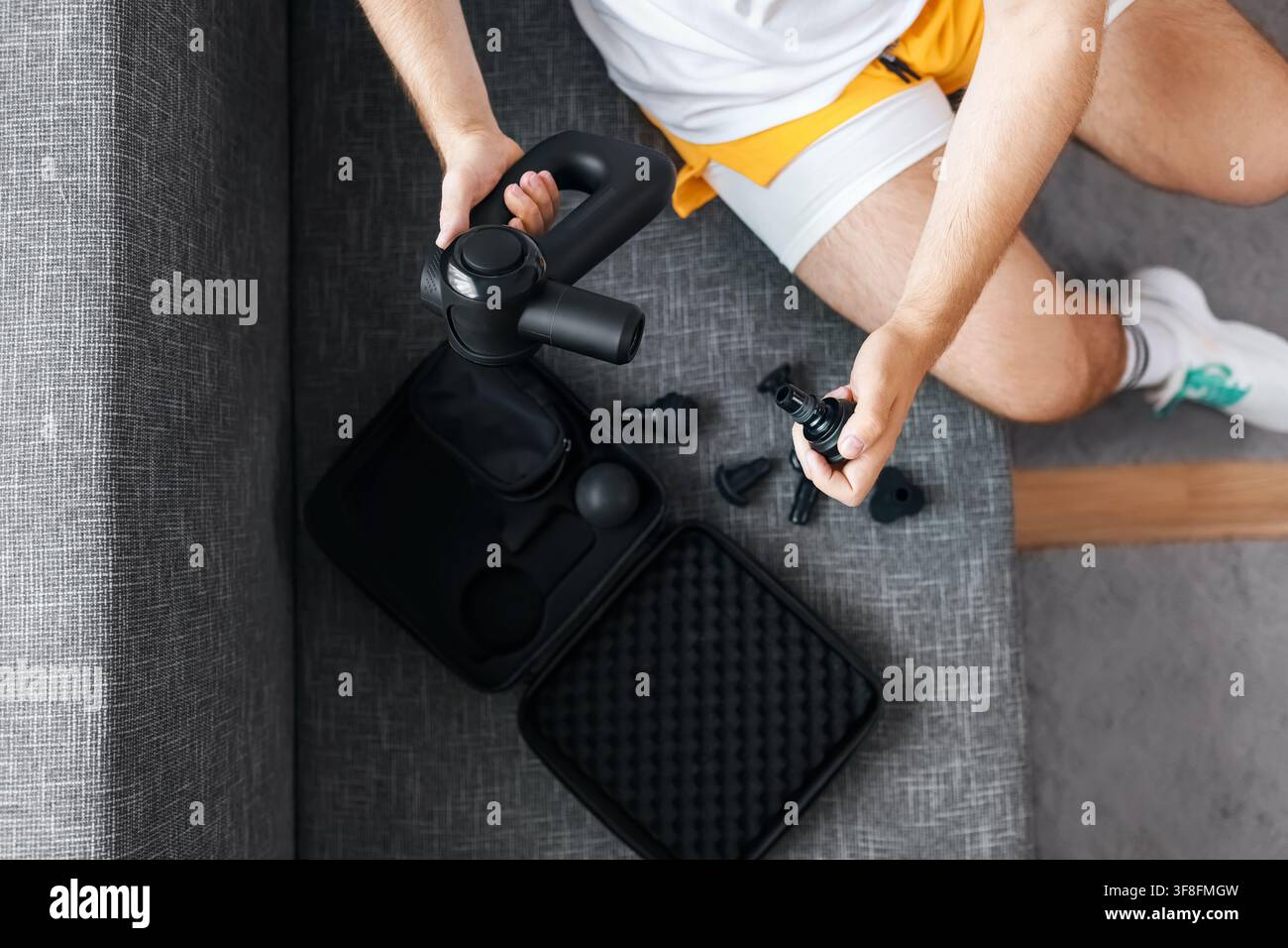 Homme changeant les accessoires d'une perceuse de massage pour la récupération post-entraînement. Thérapie physique et auto-soin pour soulager les tensions musculaires et le myofascia Banque D'Images