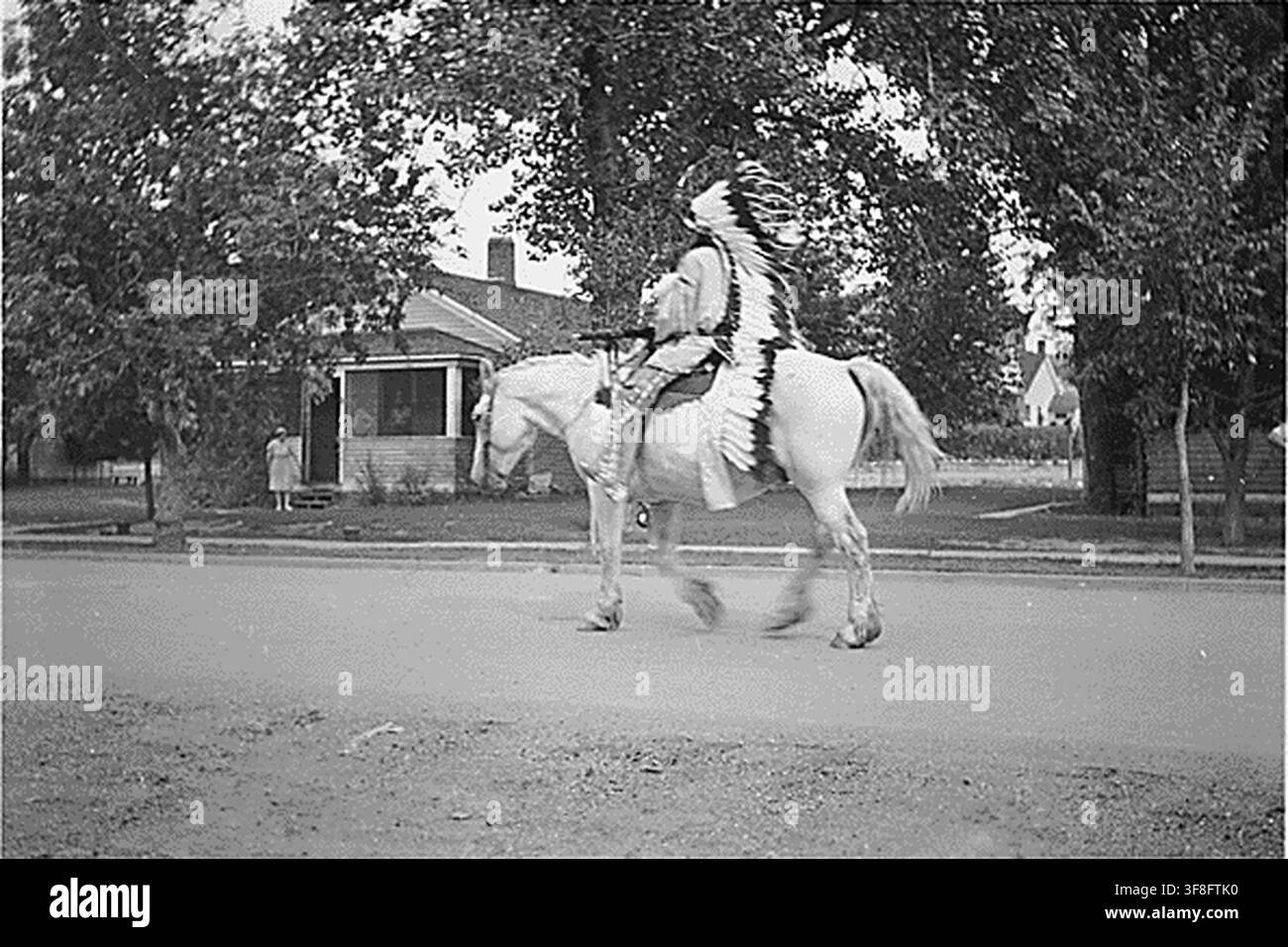 Un Indien en tenue traditionnelle monte un cheval devant des maisons, photographié en 1940, dans le cadre des archives du Bureau of Indian Affairs. Banque D'Images