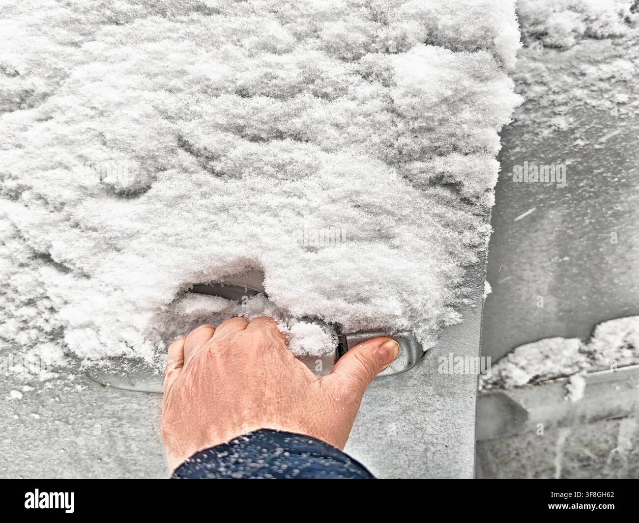 Vue rapprochée d'une personne luttant pour déverrouiller une poignée de porte de voiture recouverte de glace et de neige par temps froid d'hiver. Banque D'Images