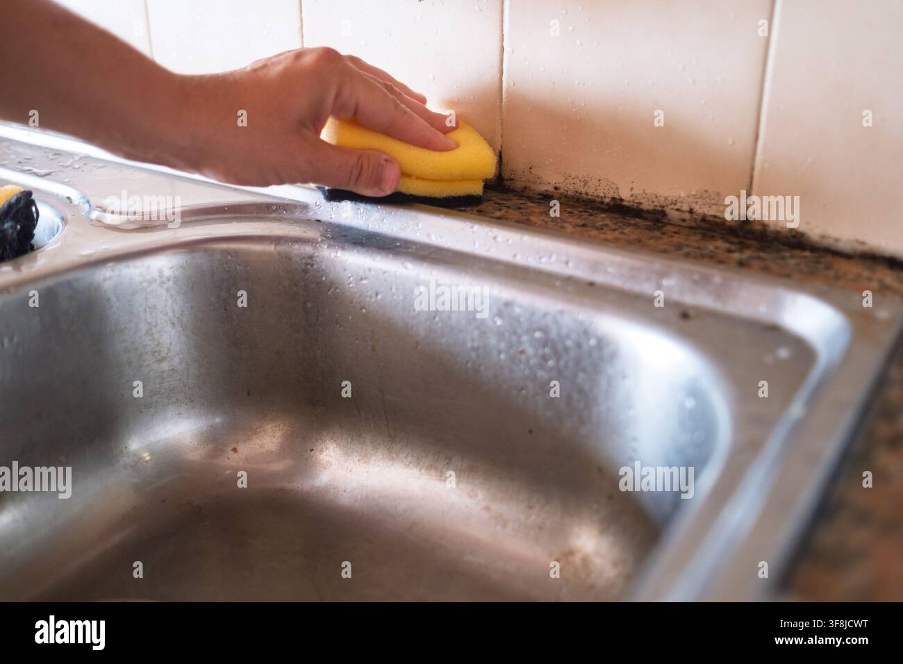 Une personne nettoyant les carreaux de l'évier de cuisine avec une éponge Banque D'Images