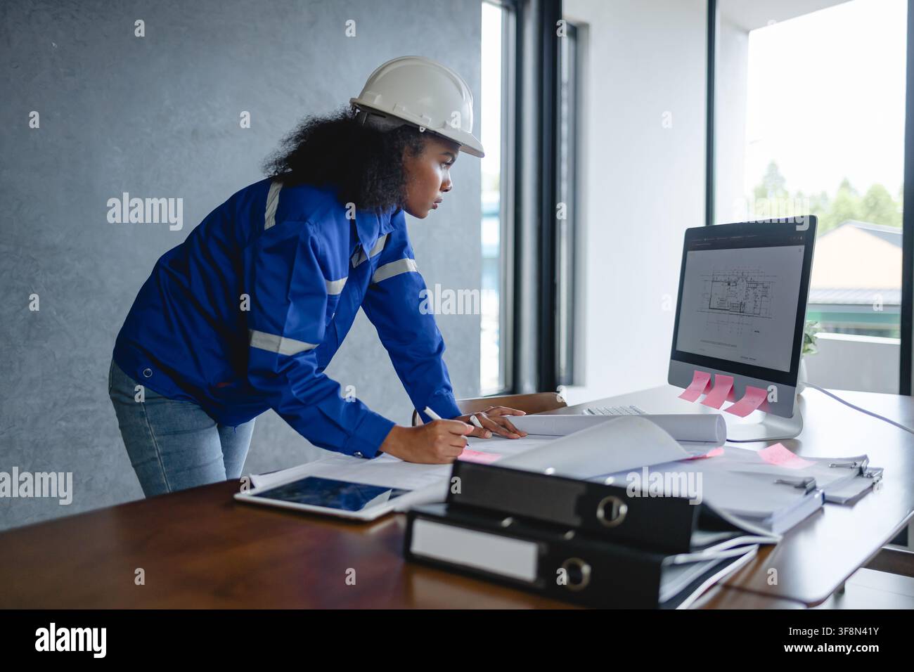 Portrait d'ingénieur portant un casque de sécurité et un uniforme devant un fond gris, paraissant concentré et professionnel, représentant. Banque D'Images
