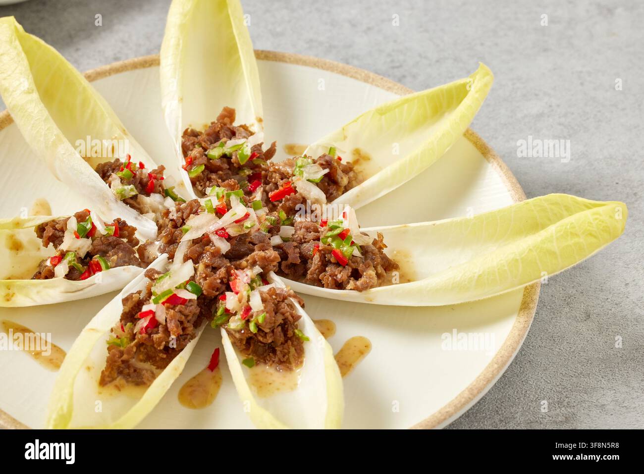 Salade de bœuf gourmet, fruits de mer saisissis dans une poêle en fonte et bouchées d'endive belge en entrée avec garniture de viande servies sur des assiettes blanches, restaurant haut de gamme fo Banque D'Images