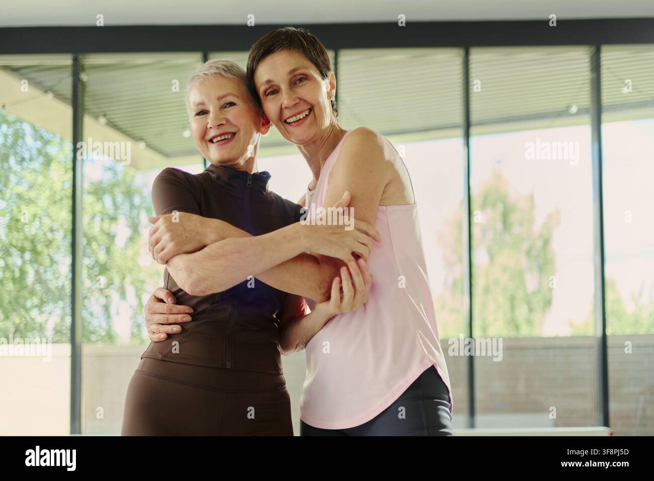 Portrait de deux femmes caucasiennes âgées s'embrassant et souriant après une séance de sport dans une salle de gym, représentant le vieillissement actif et le bien-être. Idéal pour le marketing des soins de santé et de la forme physique chez les seniors, vue en contre-plongée Banque D'Images