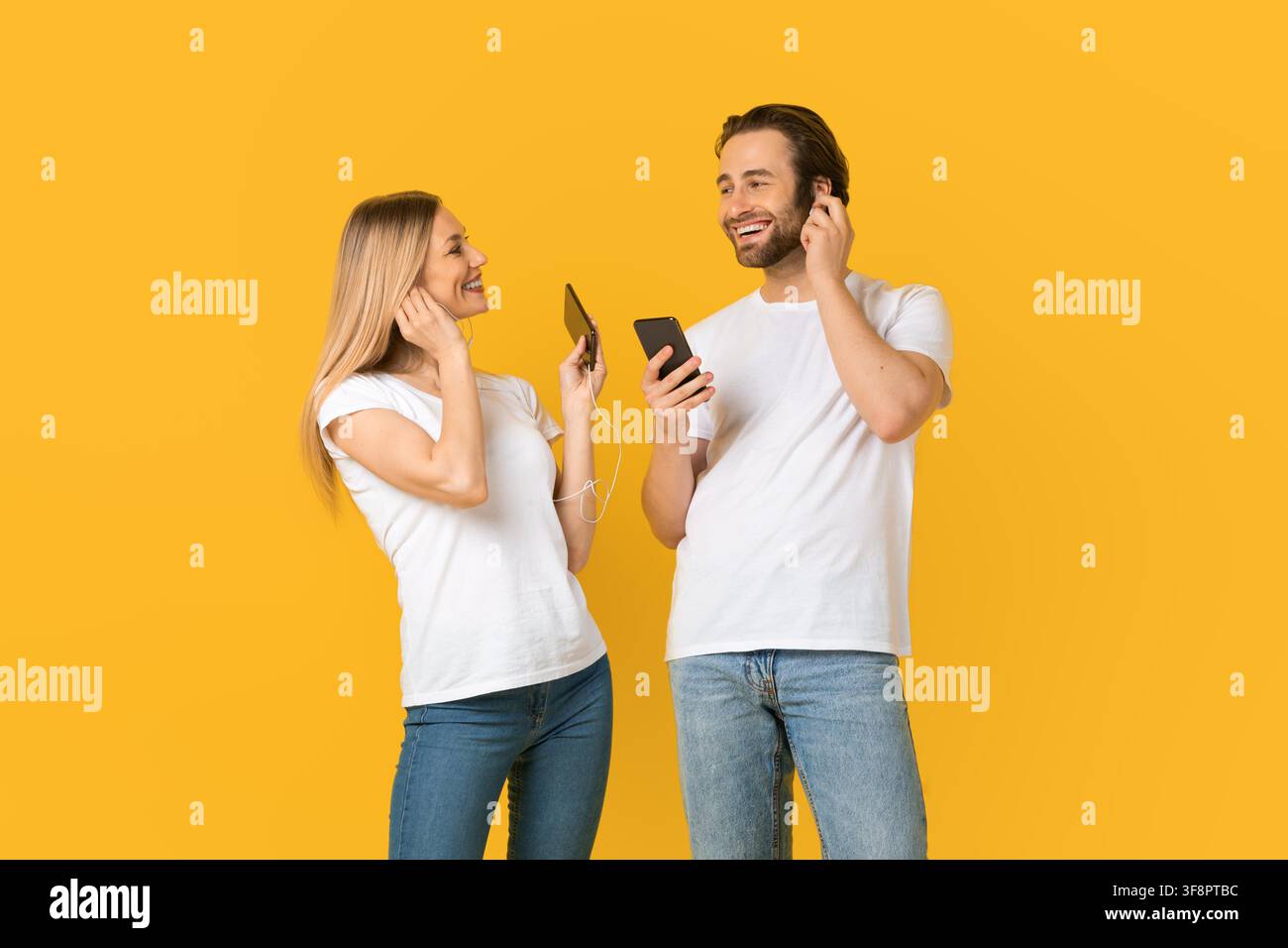 Jeun couple heureux écoutant de la musique ensemble, souriant, fond jaune Banque D'Images