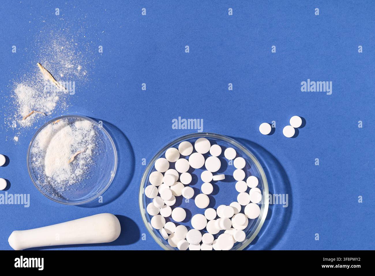 Comprimés blancs et poudre dans des boîtes de Pétri avec un mortier et un pilon sur fond bleu, concept de recherche pharmaceutique, Divers comprimés blancs sont disposés Banque D'Images