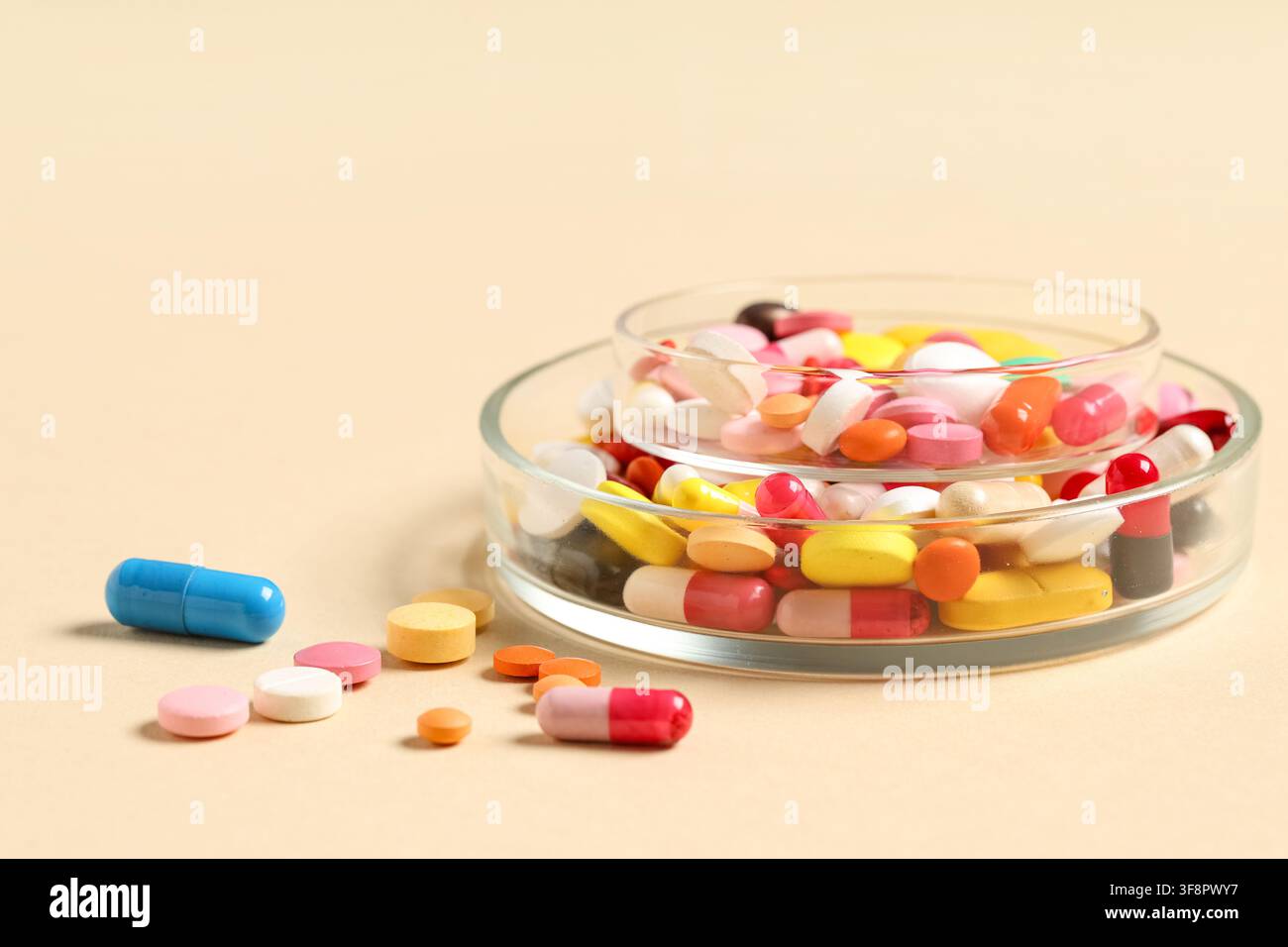 Assortiment de pilules et capsules pharmaceutiques colorées dans des boîtes de Pétri en verre sur un fond beige, soins de santé et médecine Banque D'Images