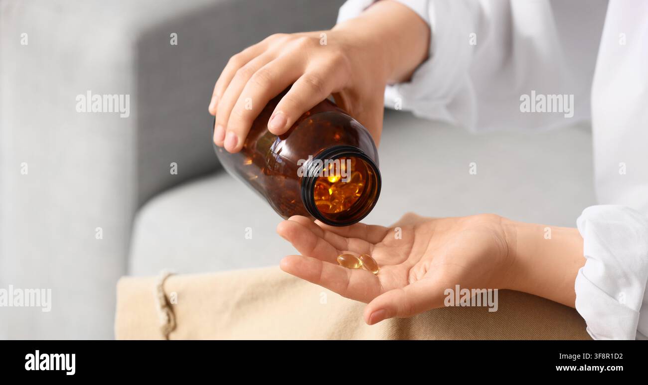 Person versant des capsules gélatineuses jaunes d'une bouteille brune dans sa main, prise quotidienne de vitamines et de suppléments pour la santé et le bien-être Banque D'Images