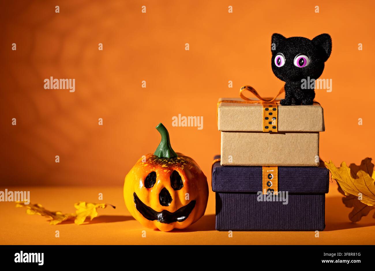 Chat noir sur des boîtes-cadeaux empilées à côté d'une lanterne de citrouille sur fond orange pour une affiche mignonne de fête d'Halloween ou une promotion de vente Banque D'Images