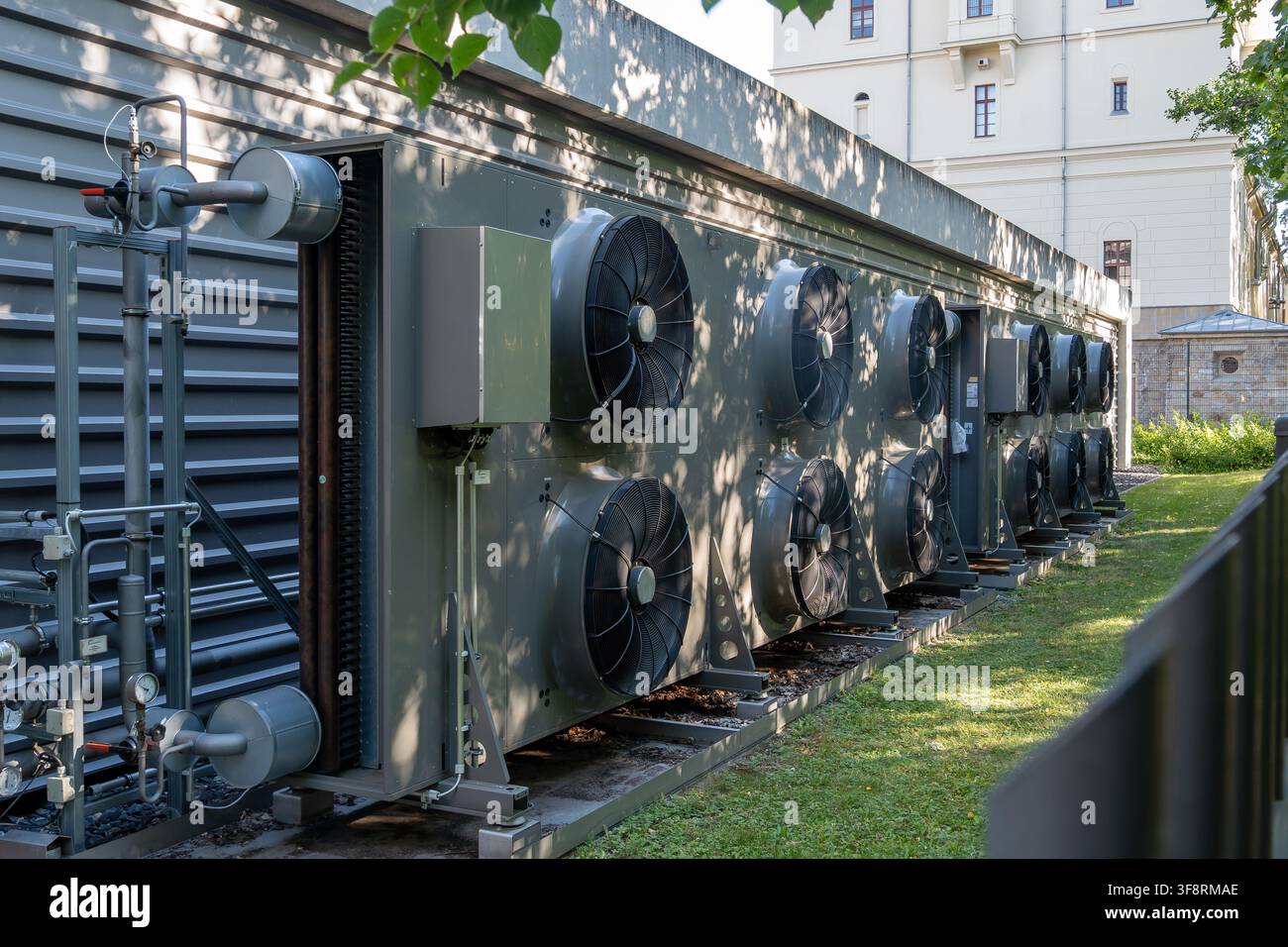 Une grande unité de pompe à chaleur air-eau industrielle installée à l'extérieur à côté d'une façade de bâtiment pour un contrôle climatique et des systèmes de chauffage efficaces. Banque D'Images