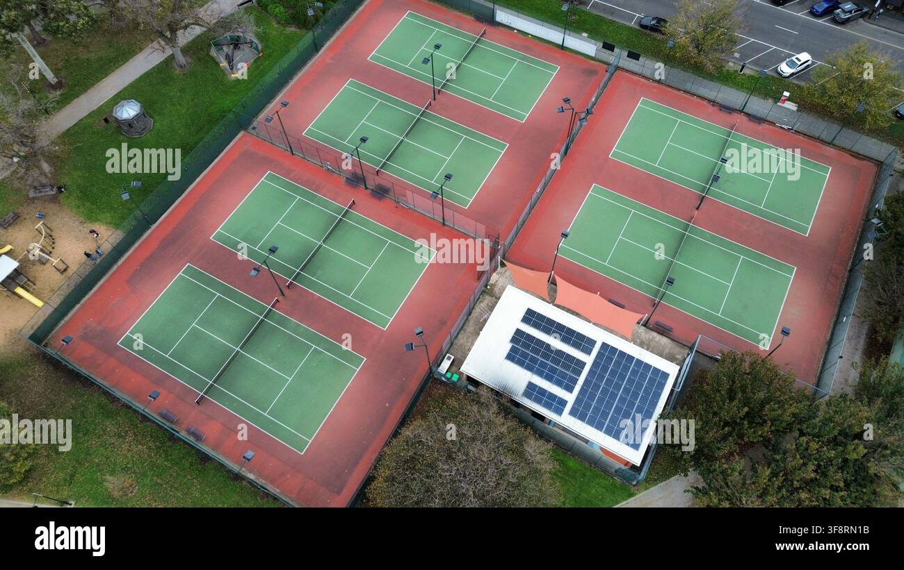Plusieurs courts de tennis avec filets et projecteurs pour les activités sportives, montrant un bâtiment doté de panneaux solaires sur le toit Banque D'Images
